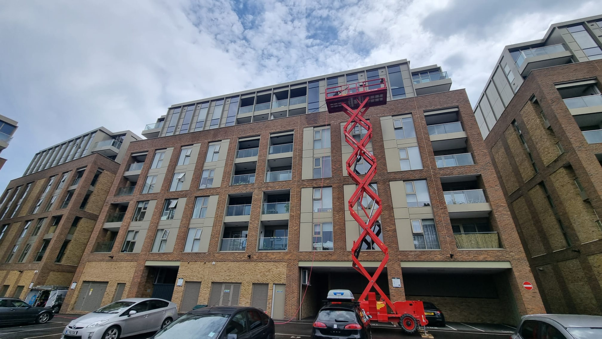 Scissor lift raised against a brick and cladding apartment block during an exterior building clean
