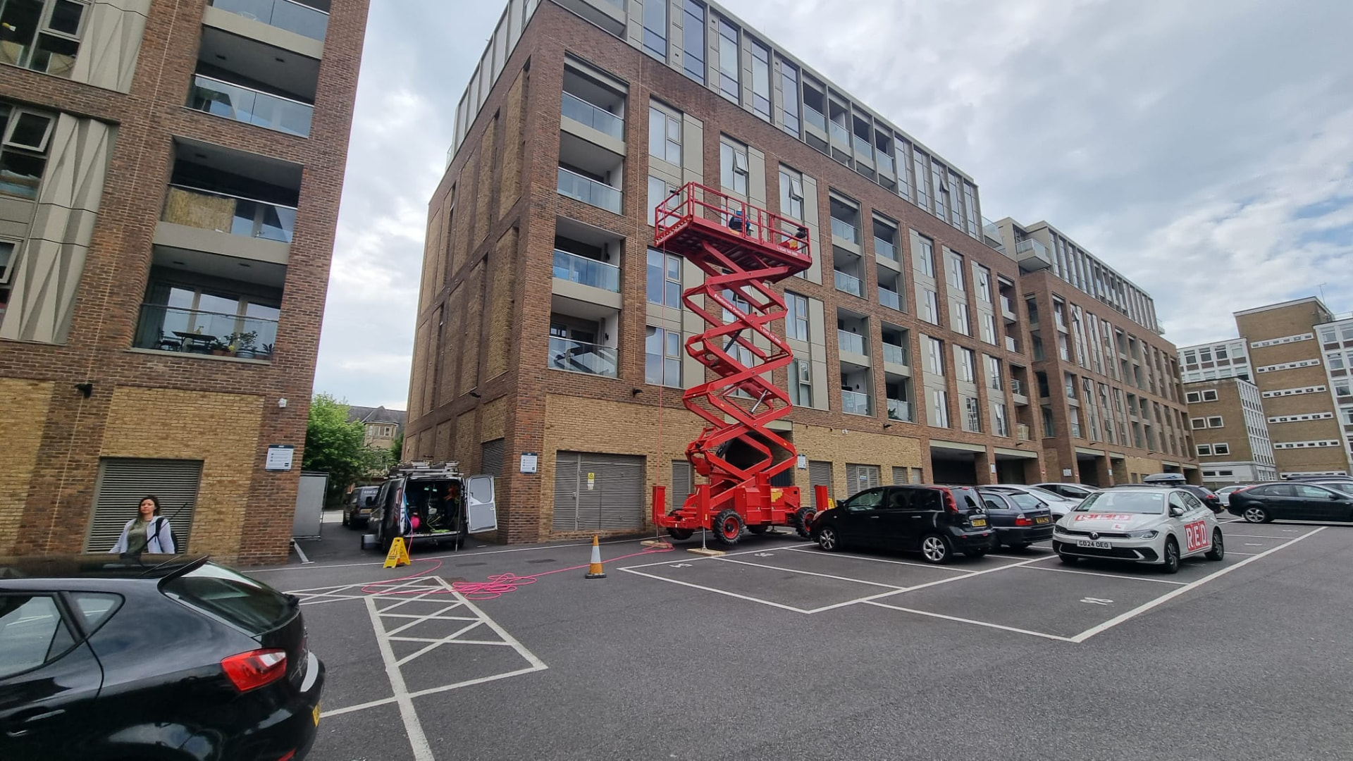 Scissor lift and work van set up in a car park beside an apartment building being cleaned
